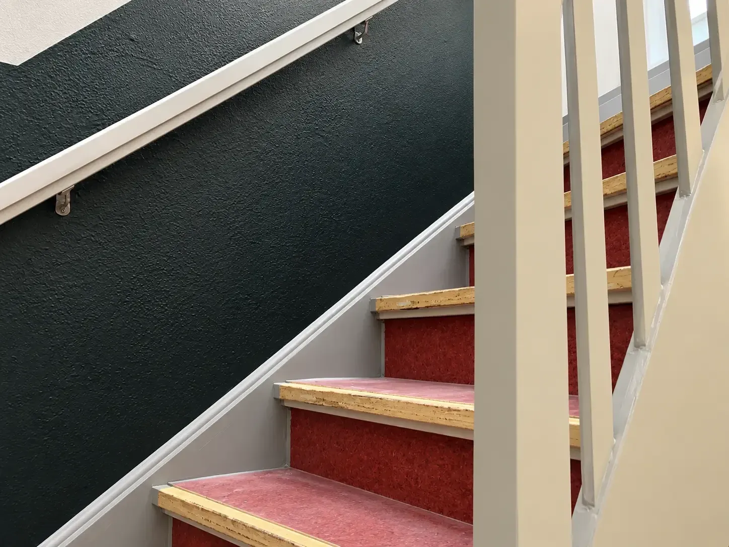 Geschilderd trappenhuis met donkere lambrisering en lichtgrijze balusters.