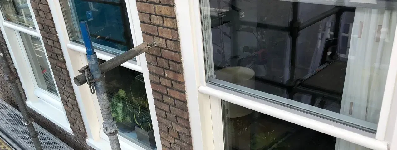 Tijdens: hetzelfde kozijn, net geschilderd, met de steiger ervoor.
